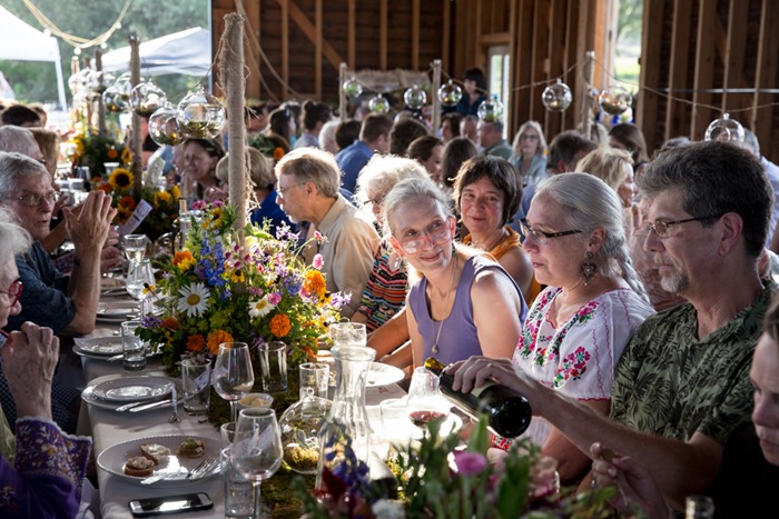 150 guests are gathered inside the barn for a farm-to-table dinner by Debra Prinzing
