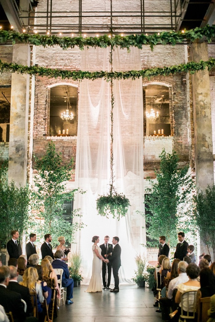 Custom garlands help make up hanging floral design at a wedding in a tall, rustic building