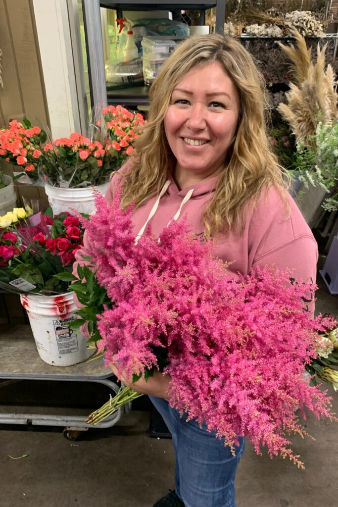 Flower Wholesale business owner Imelda Ramos standing in her warehouse holding a bouquet of astilbe.