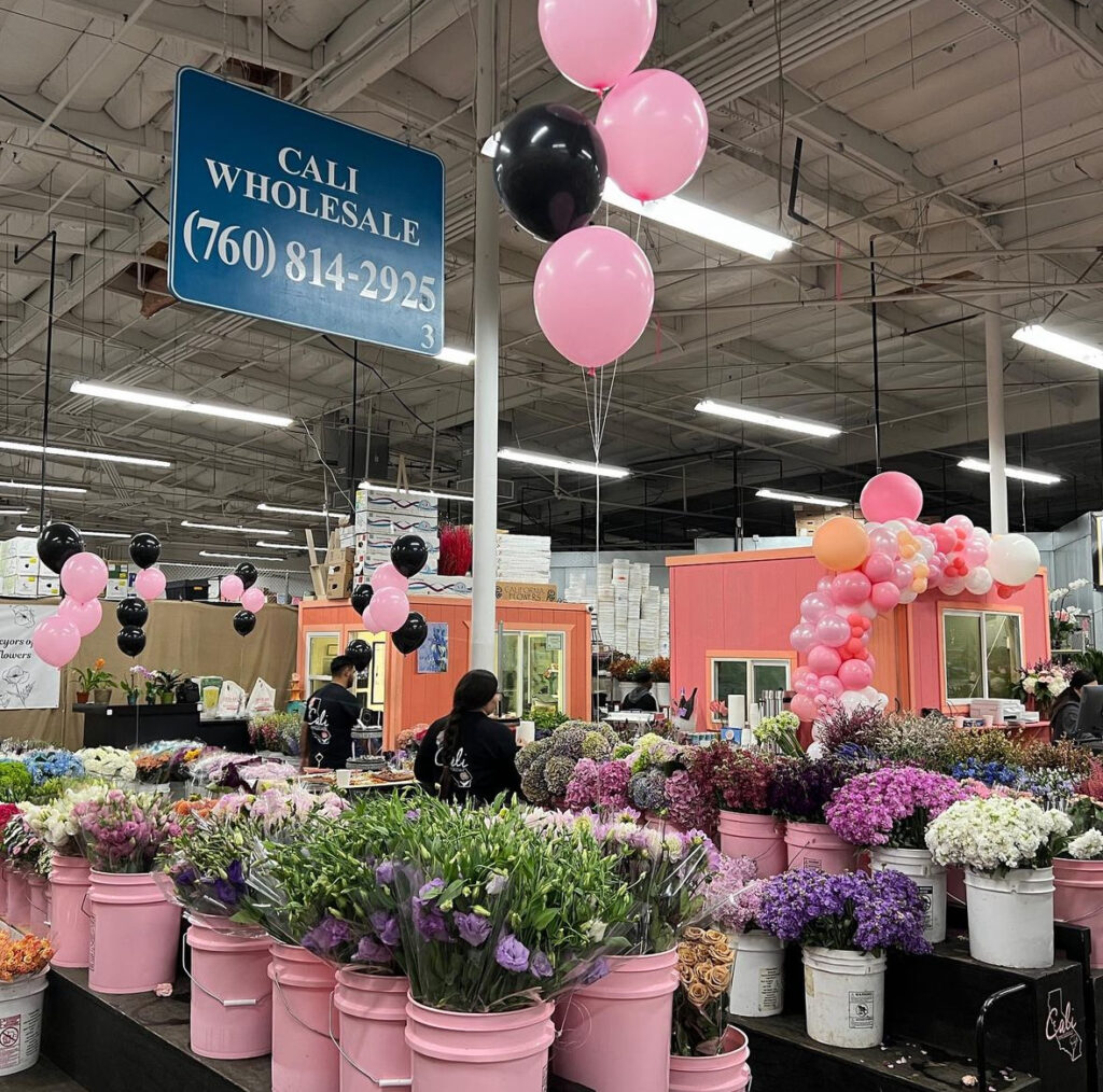 The stall of a flower wholesale business called Cali Wholesale at a California flower market with pink buckets of flowers for sale.